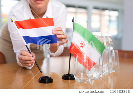 Little flag of Iran on table and flag of Netherlands put next to it by young woman 116583838