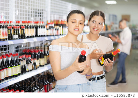 Two female friends choose soy sauce in Chinese supermarket. Read the QR code from the label using smartphone 116583878