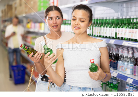Cheerful female friends choosing alcoholic beverage at store 116583885