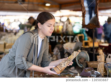 Young woman looking at figurine of virgin at flea market Young woman looking at figurine of virgin at flea market 116583887