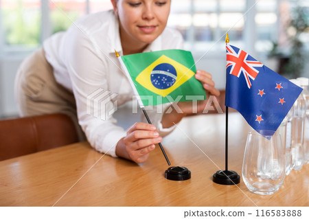 Preparing for business presentation - secretary places flags of Brazil and Australia on negotiating table Preparing for business presentation - secretary places flags of Brazil and Australia on negotiating table 116583888