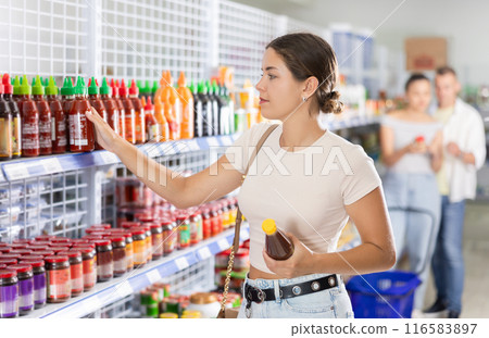 Positive female customer choosing spicy sauce in supermarket Positive female customer choosing spicy sauce in supermarket 116583897