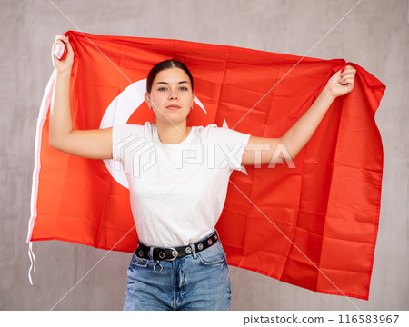 Contented young woman holding Turkey flag against unicoloured background Contented young woman holding Turkey flag against unicoloured background 116583967