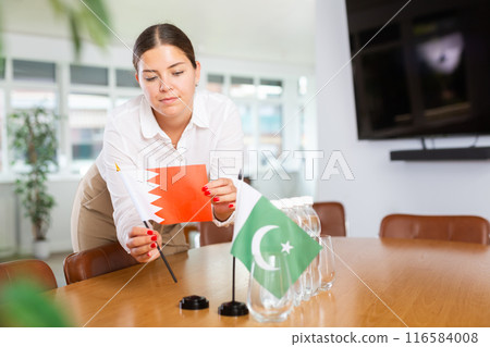 Young woman putting flags of Qatar and Pakistan on table in office 116584008