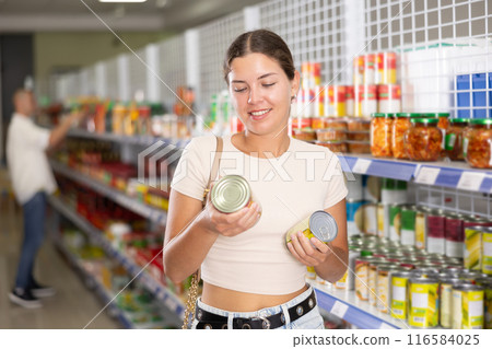 Young woman choosing canned food in store 116584025