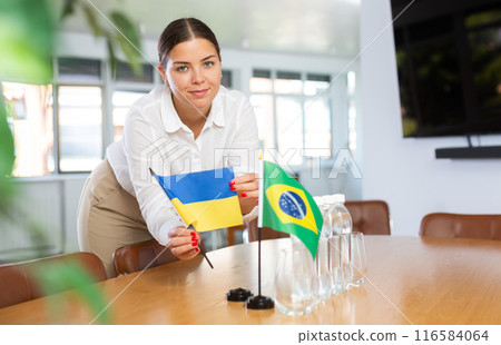 Positive young woman putting little flag of Ukraine on table next to the flag of Brazil 116584064