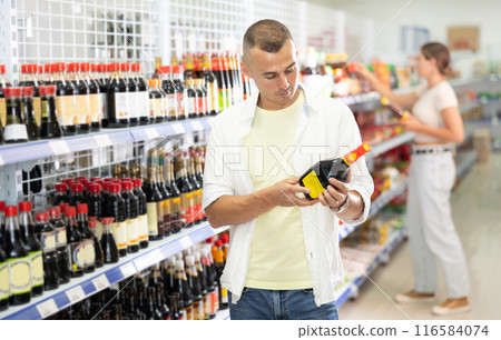 Portrait of male customer choosing soy sauces in grocery food shop 116584074