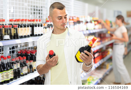 Young man choosing soy sauce in store 116584169