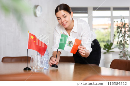 Young female attendant putting up flags for international negotiations between china and mexico Young female attendant putting up flags for international negotiations between china and mexico 116584212