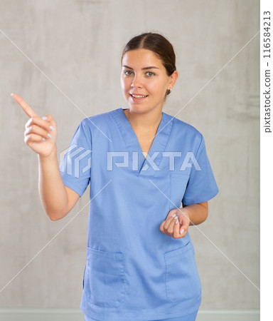 Emotional woman portrait of a nurse wearing a blue coat looking into the camera on grey background, space for text Emotional woman portrait of a nurse wearing a blue coat looking into the camera on grey background, space for text 116584213
