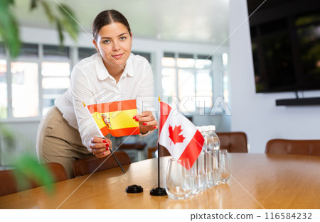 Positive young woman putting little flag of Spain on table next to the flag of Canada 116584232