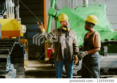Medium long shot of two ethnically diverse male and female engineers working in heavy machinery production industry having conversation Medium long shot of two ethnically diverse male and female engineers working in heavy machinery production industry having conversation 116584560