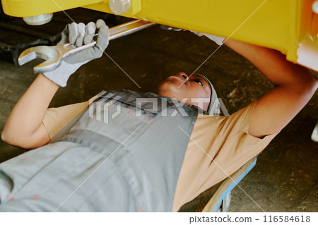 Medium closeup modern young African American female technician repairing bottom part of industrial machine Medium closeup modern young African American female technician repairing bottom part of industrial machine 116584618