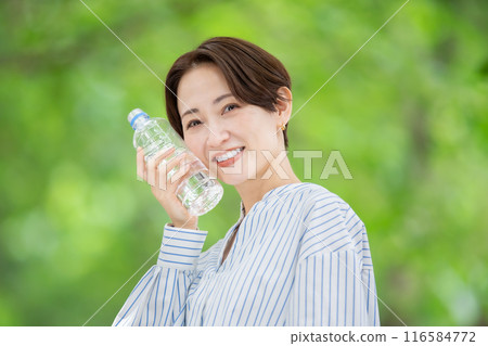 Woman holding a plastic bottle, fresh greenery 116584772