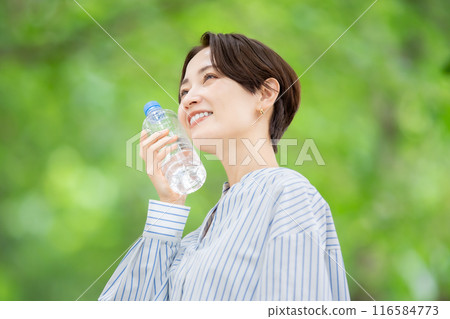 Woman holding a plastic bottle, fresh greenery 116584773