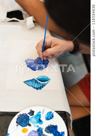 Close-up of a woman brush painting elements of the sea with a color palette beside her. Vertical Close-up of a woman brush painting elements of the sea with a color palette beside her. Vertical 116584836
