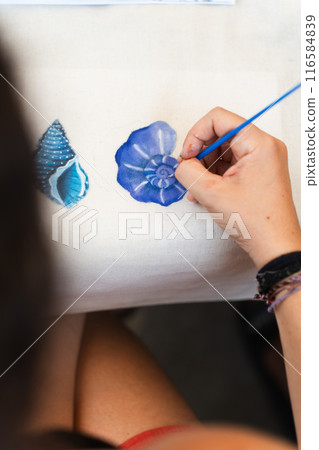 Woman hand painting elements of the sea with a brush in a workshop. Vertical 116584839