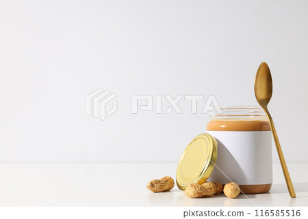 Peanut paste in a glass jar with a spoon, on a light background. 116585516