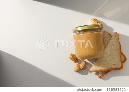 Peanut paste in a glass jar with toast, on a light background. 116585521