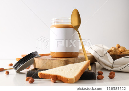 Peanut paste in a glass jar with a spoon, on a light background. 116585522