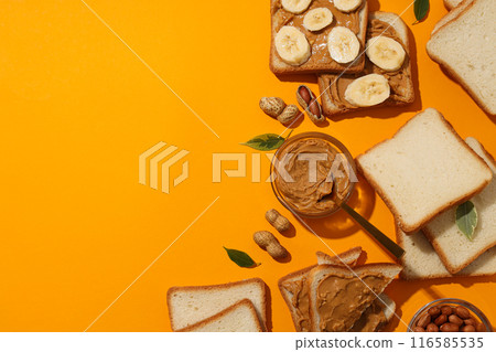 Peanut paste in a jar with sandwiches next to it on a yellow background. 116585535