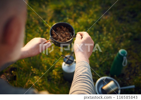 High angle view closeup of unrecognizable male tourist heating up dinner with use of portable oven High angle view closeup of unrecognizable male tourist heating up dinner with use of portable oven 116585843