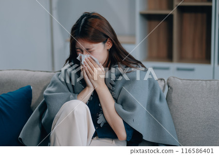 A woman with a cold with pills is treated at home chooses which drugs to take and self-medicates, checks the expiration date while sitting on the couch at home 116586401