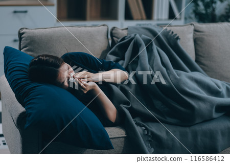 A woman with a cold with pills is treated at home chooses which drugs to take and self-medicates, checks the expiration date while sitting on the couch at home A woman with a cold with pills is treated at home chooses which drugs to take and self-medicates, checks the expiration date while sitting on the couch at home 116586412