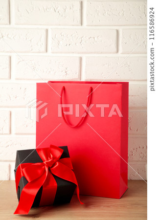 Red shopping bag with gift on light background. Black friday Red shopping bag with gift on light background. Black friday 116586924