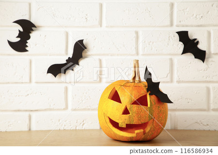 Carved glowing pumpkin and black bats on light background. Halloween celebration Carved glowing pumpkin and black bats on light background. Halloween celebration 116586934