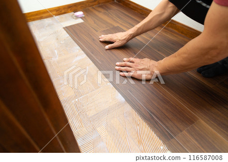 A wallpaper craftsman laying floor tiles on the hallway floor during the renovation of a used house A wallpaper craftsman laying floor tiles on the hallway floor during the renovation of a used house 116587008