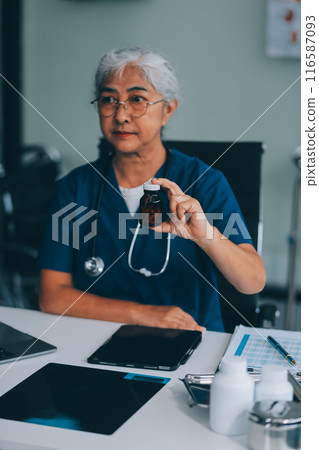 A woman doctor is writing on a clipboard and holding a bottle of pills. She is smiling and seems to be in a good mood A woman doctor is writing on a clipboard and holding a bottle of pills. She is smiling and seems to be in a good mood 116587093