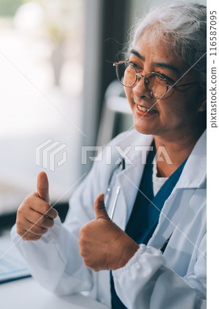Confident female doctor sitting with laptop at desk in clinic Confident female doctor sitting with laptop at desk in clinic 116587095