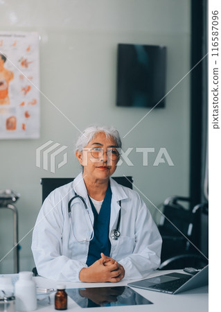 Confident female doctor sitting with laptop at desk in clinic 116587096