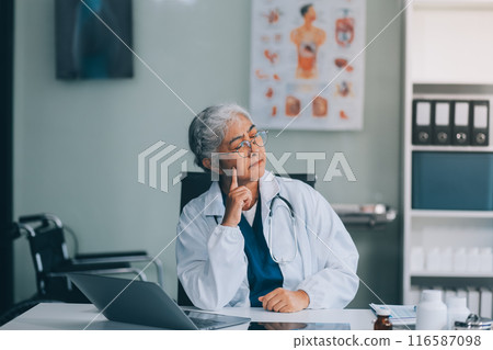 Confident female doctor sitting with laptop at desk in clinic 116587098