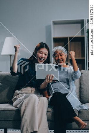 Happy grownup daughter showing content on tablet to mature mother. Two family generations women with digital computer gadget resting on couch together, watching videos, making video call Happy grownup daughter showing content on tablet to mature mother. Two family generations women with digital computer gadget resting on couch together, watching videos, making video call 116587553