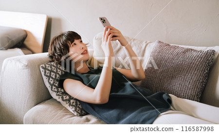 Smiling woman using a smartphone on the sofa Smiling woman using a smartphone on the sofa 116587998