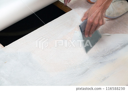 A wallpaper craftsman laying floor tiles on the wet area of a used house during renovation 116588230
