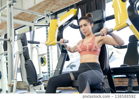 Young woman using gym machine to work on her arms strength during her morning workout at a local gym 116588592