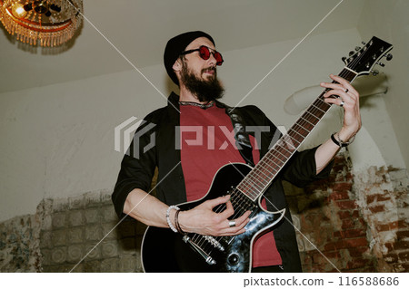Low angle view of Caucasian rock musician with beard on face playing electric guitar in room at abandoned house 116588686