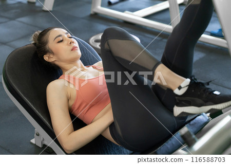 Young beautiful woman taking a rest after her leg push up exercise during her morning work out at a gym 116588703