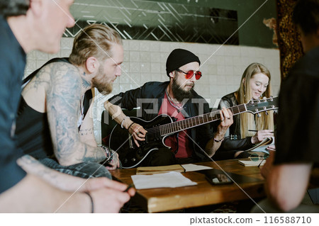 Group of Caucasian friends sitting at coffee table enjoying writing song for their new rock music album Group of Caucasian friends sitting at coffee table enjoying writing song for their new rock music album 116588710