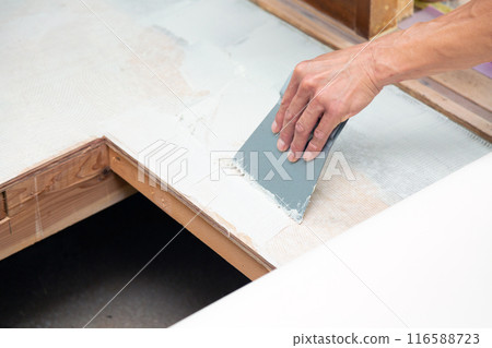 A wallpaper craftsman laying floor tiles on the wet area of a used house during renovation A wallpaper craftsman laying floor tiles on the wet area of a used house during renovation 116588723