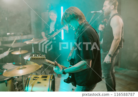 Selective focus medium shot of punk rock musician playing electric guitar in band on stage, copy space 116588787