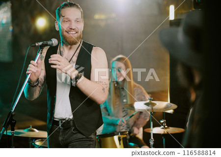 Medium shot of bearded punk rock vocalist looking at unrecognizable musician and smiling during live show 116588814
