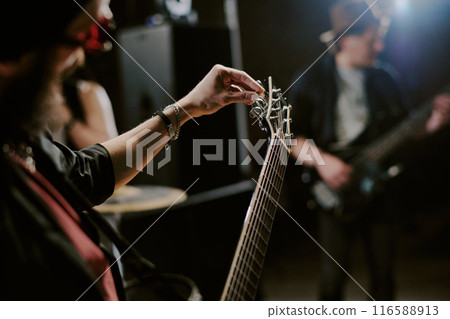 Medium closeup of unrecognizable bearded musician playing in rock band tuning electric guitar, copy space 116588913
