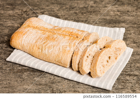 Assortment of freshly sliced baked bread with napkin on rustic table top view. Healthy unleavened bread. French bread slice Assortment of freshly sliced baked bread with napkin on rustic table top view. Healthy unleavened bread. French bread slice 116589554