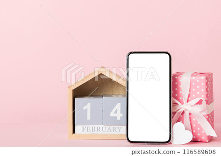 mobile phone with blank screen on colored background with hearts, calendar and gift box, valentine day 14 february concept perspertive view flat lay mobile phone with blank screen on colored background with hearts, calendar and gift box, valentine day 14 february concept perspertive view flat lay 116589608