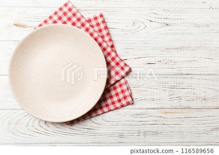 Top view on colored background empty round white plate on tablecloth for food. Empty dish on napkin with space for your design Top view on colored background empty round white plate on tablecloth for food. Empty dish on napkin with space for your design 116589656