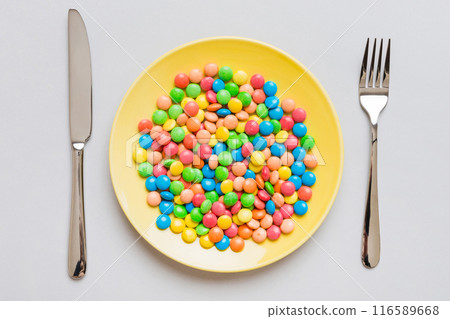 cutlery on table and sweet plate of candy. Health and obesity concept, top view on colored background cutlery on table and sweet plate of candy. Health and obesity concept, top view on colored background 116589668